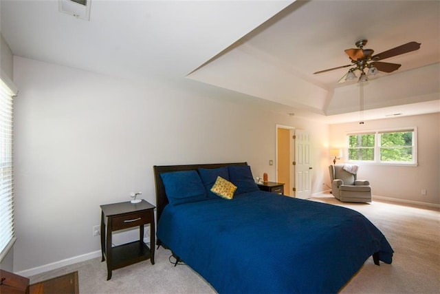 bedroom featuring light carpet, a raised ceiling, baseboards, and a ceiling fan