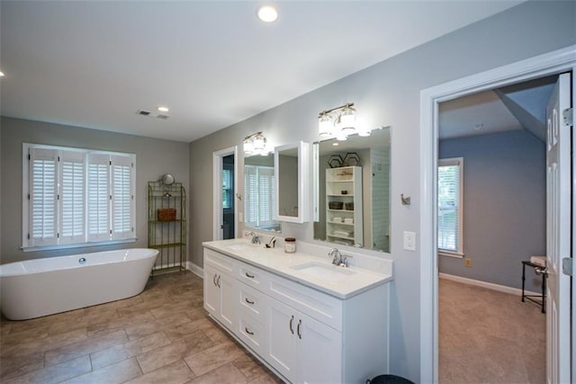 full bath with baseboards, a freestanding bath, double vanity, and recessed lighting