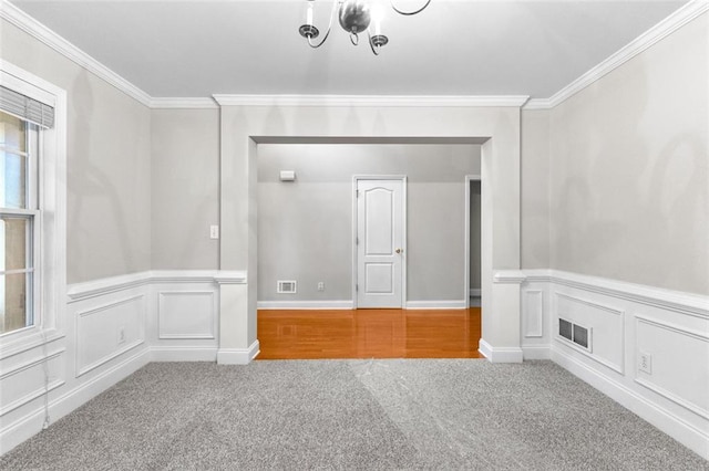 empty room with ornamental molding, carpet, visible vents, and a decorative wall