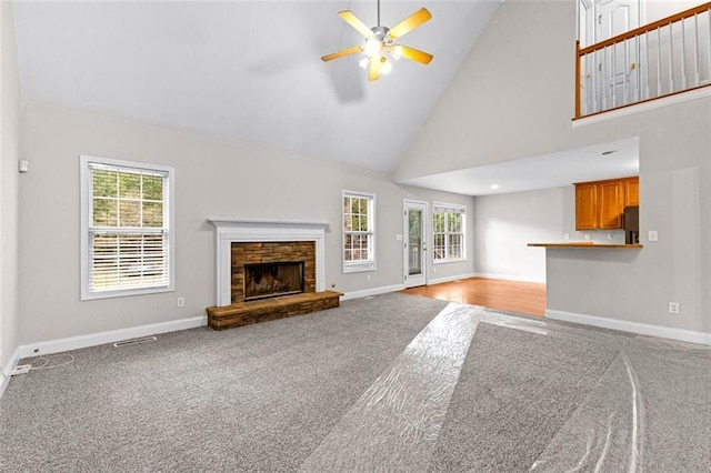 unfurnished living room featuring carpet floors, high vaulted ceiling, a stone fireplace, and baseboards