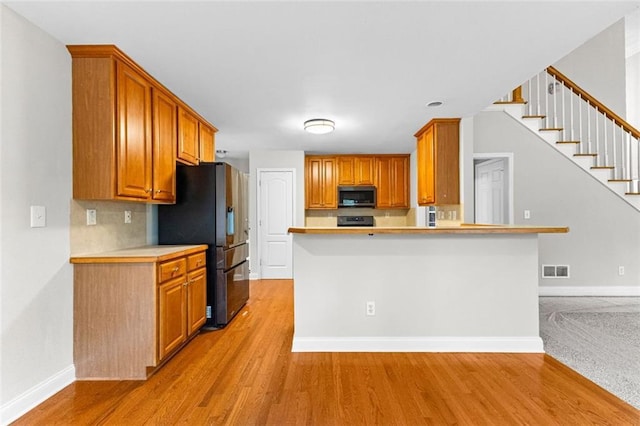 kitchen featuring baseboards, light wood-style flooring, stainless steel microwave, light countertops, and refrigerator with ice dispenser