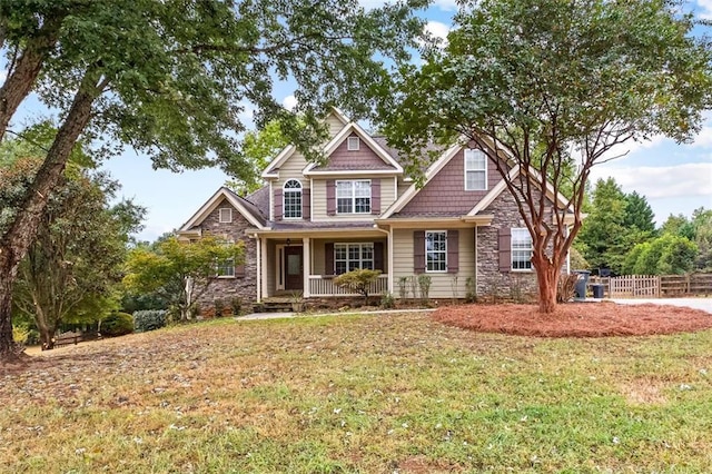 craftsman inspired home with stone siding, covered porch, fence, and a front lawn