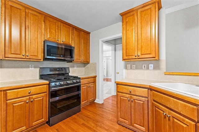 kitchen featuring light wood finished floors, stainless steel appliances, light countertops, and brown cabinetry