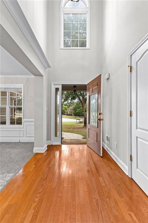 entrance foyer with a wealth of natural light, visible vents, a towering ceiling, and hardwood / wood-style floors