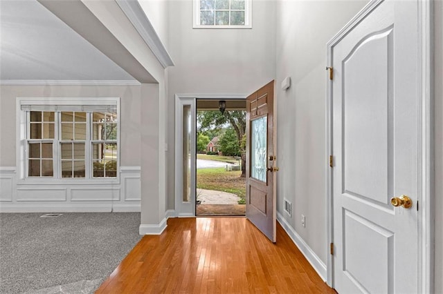 entryway featuring light carpet, ornamental molding, plenty of natural light, and a decorative wall