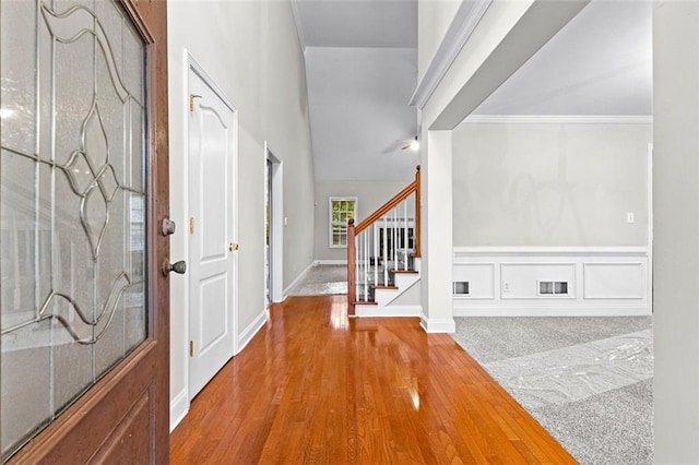 entrance foyer featuring visible vents, wood finished floors, stairs, crown molding, and a decorative wall