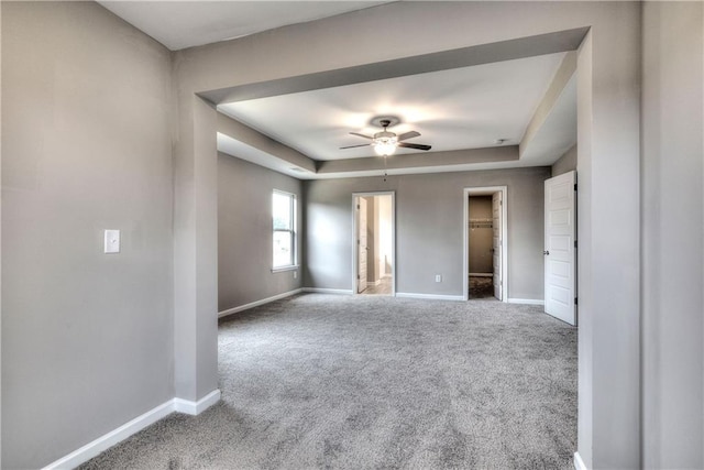 carpeted empty room with a ceiling fan, baseboards, and a tray ceiling