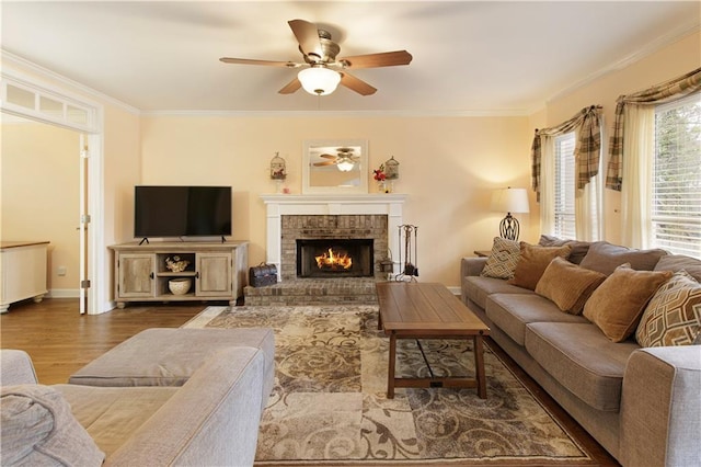 living area featuring wood finished floors, a fireplace, ornamental molding, and a ceiling fan