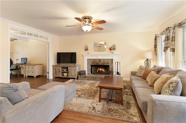 living room featuring a ceiling fan, wood finished floors, crown molding, baseboards, and a brick fireplace