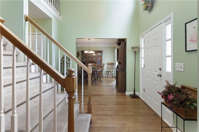 foyer entrance with stairway, an inviting chandelier, wood finished floors, and a towering ceiling