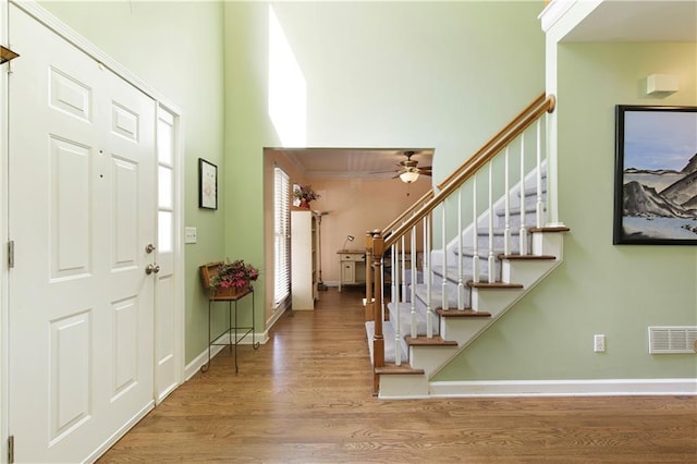 entrance foyer featuring visible vents, a ceiling fan, wood finished floors, stairway, and baseboards