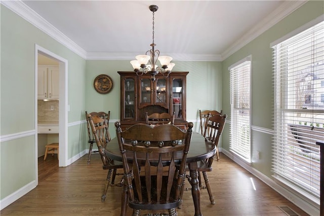 dining space featuring visible vents, crown molding, baseboards, a chandelier, and wood finished floors