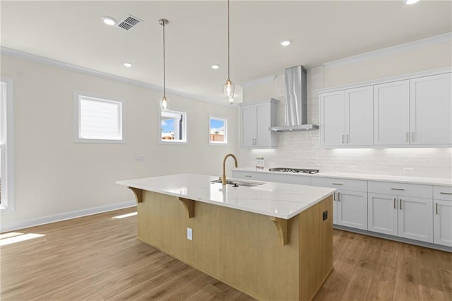 kitchen with ornamental molding, a sink, wall chimney range hood, gas cooktop, and a kitchen breakfast bar