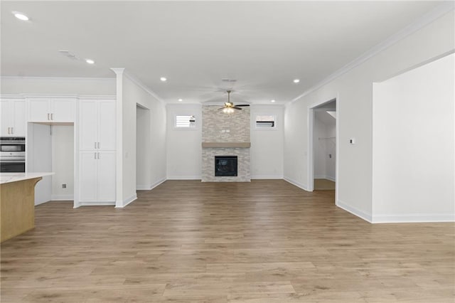 unfurnished living room featuring a ceiling fan, a fireplace, light wood finished floors, and ornamental molding