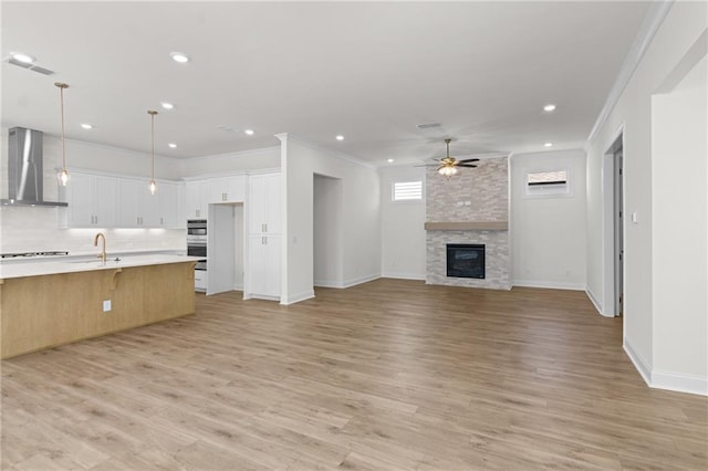 unfurnished living room featuring a ceiling fan, crown molding, a fireplace, and light wood finished floors