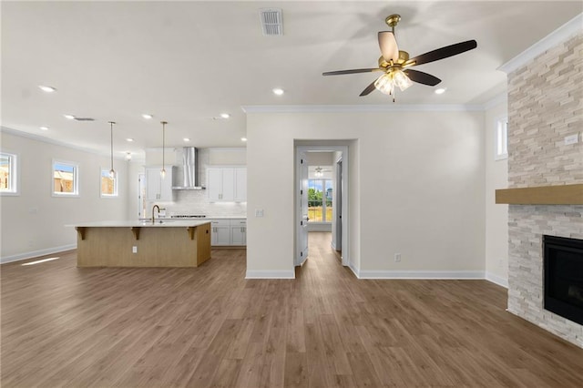 kitchen with a breakfast bar area, a fireplace, visible vents, open floor plan, and wall chimney exhaust hood