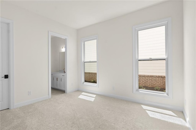 unfurnished bedroom with light colored carpet, ensuite bathroom, baseboards, and multiple windows