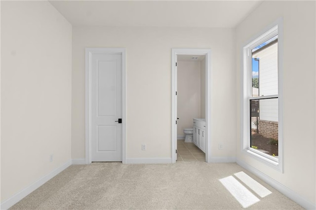 unfurnished bedroom featuring ensuite bath, baseboards, and light colored carpet