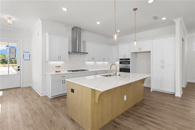 kitchen with a sink, visible vents, white cabinets, wall chimney exhaust hood, and stovetop