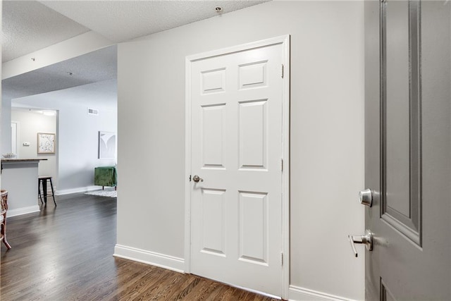 hallway featuring visible vents, baseboards, a textured ceiling, and dark wood-style floors