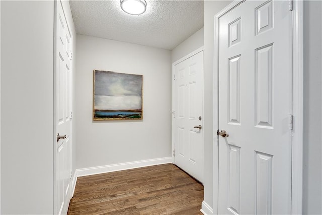 hallway with dark wood-style floors, a textured ceiling, and baseboards