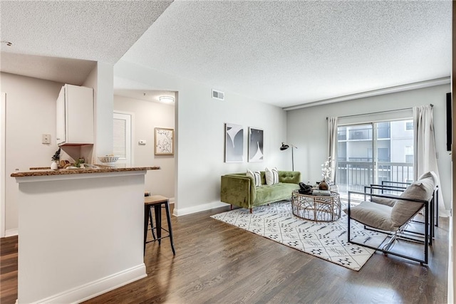 living room with dark wood-style floors, visible vents, a textured ceiling, and baseboards