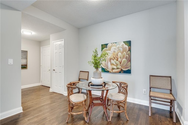 dining space with baseboards, a textured ceiling, and wood finished floors