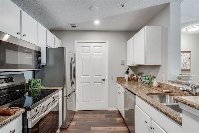 kitchen with a sink, a textured ceiling, white cabinetry, stainless steel appliances, and dark wood-style flooring