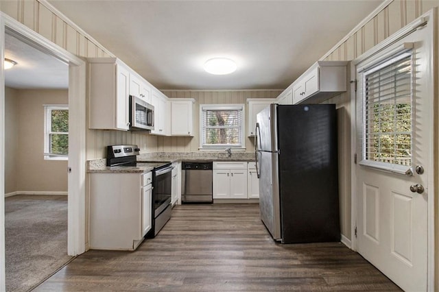 kitchen featuring appliances with stainless steel finishes, white cabinetry, sink, dark hardwood / wood-style flooring, and dark stone counters