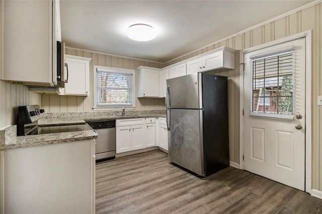 kitchen featuring white cabinetry, crown molding, hardwood / wood-style flooring, stainless steel appliances, and light stone countertops