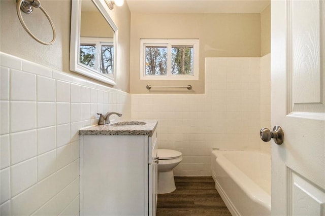 bathroom with toilet, tile walls, vanity, hardwood / wood-style flooring, and a washtub