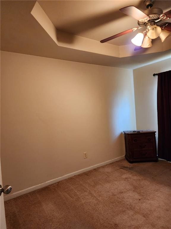 carpeted spare room featuring a raised ceiling and ceiling fan