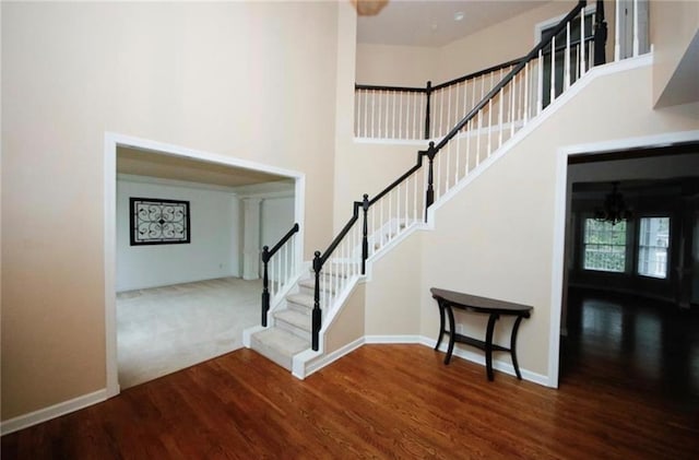 staircase with a chandelier, a towering ceiling, and wood-type flooring