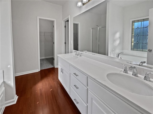 bathroom with double vanity, a shower stall, a sink, and wood finished floors