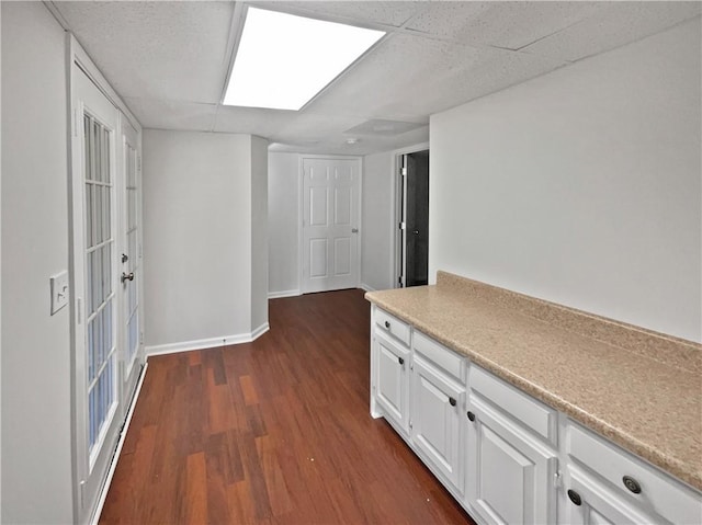 interior space with a paneled ceiling, baseboards, and dark wood finished floors