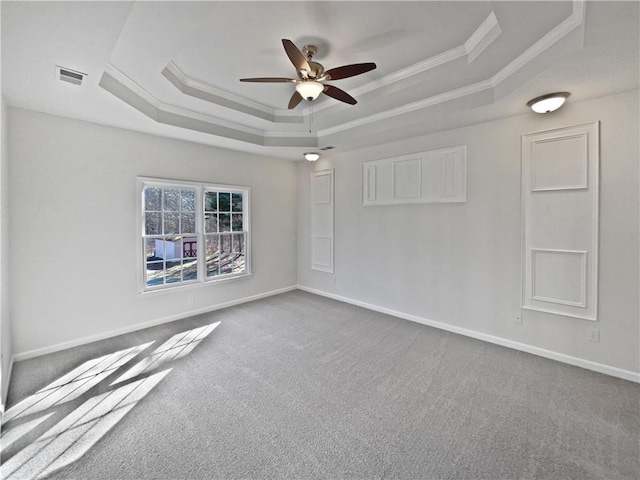 carpeted spare room featuring visible vents, a ceiling fan, baseboards, ornamental molding, and a tray ceiling