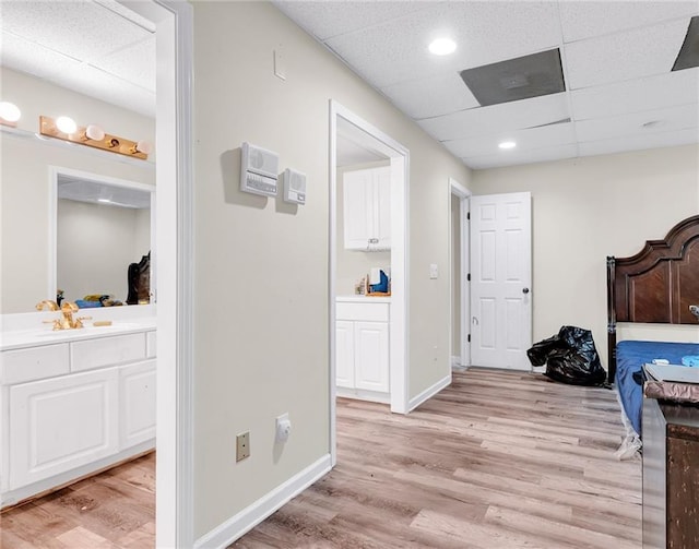 bedroom featuring light wood-style floors, baseboards, ensuite bathroom, and a paneled ceiling