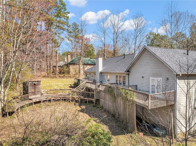 back of house with a wooden deck, french doors, a chimney, and a shingled roof