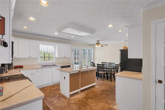 kitchen featuring stainless steel gas cooktop, a kitchen island, freestanding refrigerator, light countertops, and white cabinets