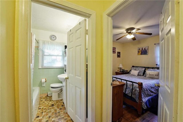 bedroom featuring ceiling fan, tile walls, and ensuite bath