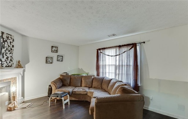 living room featuring dark wood-type flooring, a brick fireplace, and a textured ceiling