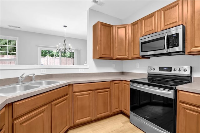 kitchen with appliances with stainless steel finishes, a sink, a chandelier, light wood-style flooring, and light countertops