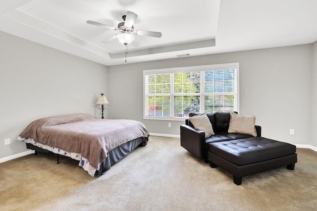 carpeted bedroom with a raised ceiling, baseboards, and ceiling fan