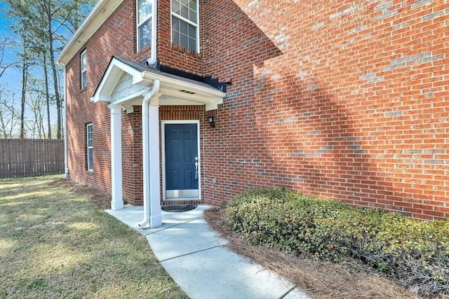 doorway to property featuring fence and brick siding