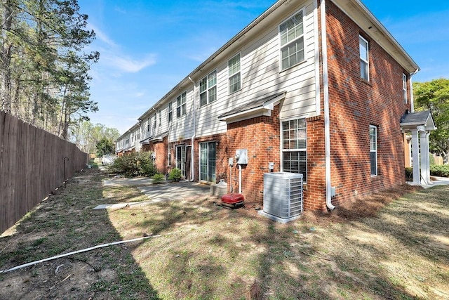 rear view of house with central AC unit, brick siding, a patio, and fence