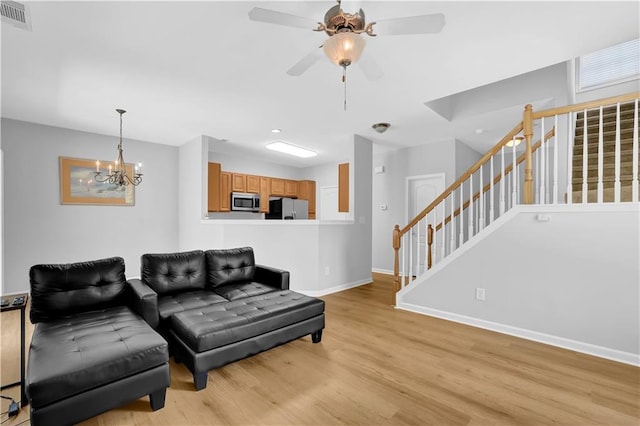 living area with baseboards, light wood-type flooring, ceiling fan, a chandelier, and stairway