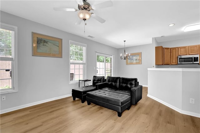 living room featuring light wood finished floors, a chandelier, baseboards, and ceiling fan