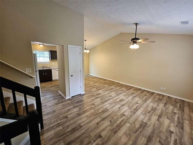 unfurnished living room with ceiling fan, lofted ceiling, sink, a textured ceiling, and hardwood / wood-style flooring