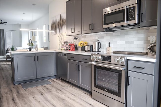 kitchen featuring gray cabinetry, stainless steel appliances, kitchen peninsula, and light wood-type flooring