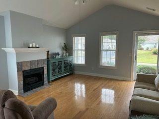 living area featuring a tile fireplace, baseboards, lofted ceiling, and wood finished floors